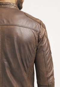 Brun läderjacka med en texturerad yta, med en klassisk krage, sömmar och en figursydd skärning. Bakvy visar axeldesignen.