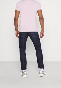 Mörkblå jeans med slim fit, kombinerat med en ljusrosa T-shirt. Outfiten avslutas med vita och silverfärgade sneakers.