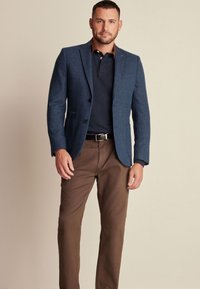 Laivastonsininen bleiseri, joka on tehty teksturoidusta kankaasta, slim fit -mallilla, yksirivisellä muotoilulla ja kahdella etutaskulla, yhdistettynä ruskeisiin chinopö pantsuihin.