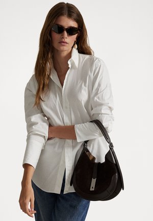 Black leather handbag with a curved shape, smooth texture, and a silver hardware accent. Model wears a white shirt and sunglasses.