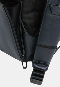 Sezione della borsa in pelle blu navy che mostra una tasca con zip, rivestimento in tessuto testurizzato e una robusta tracolla regolabile con accessori in metallo.