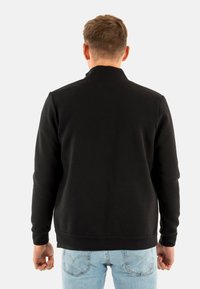 Felpa nera con collo alto, maniche lunghe e polsini a coste, abbinata a jeans azzurri, vista da dietro.