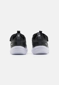 Baskets de sport noires avec une tige en tissu texturé, semelle en caoutchouc blanche, onglets de traction et un détail de logo discret sur le talon.