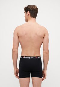 Sorte boxershorts med en Champion elastisk midjebånd, glatt stoff og en tettsittende design, vist fra baksiden på en mannlig modell.