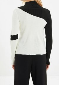 Jersey acanalado con cuello alto, con un diseño gráfico en blanco y negro; la parte trasera tiene bloques de color contrastantes y tela texturizada.