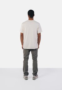 Helles beige T-Shirt mit Rundhalsausschnitt, kurzen Ärmeln und geradem Schnitt, kombiniert mit grauen Hosen und grauen Sneakers.