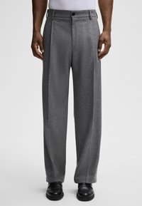 Szare spodnie w kant z fakturowanym wykończeniem, z zapięciem na guzik i szerokimi nogawkami, które zestawiono z czarnymi butami.