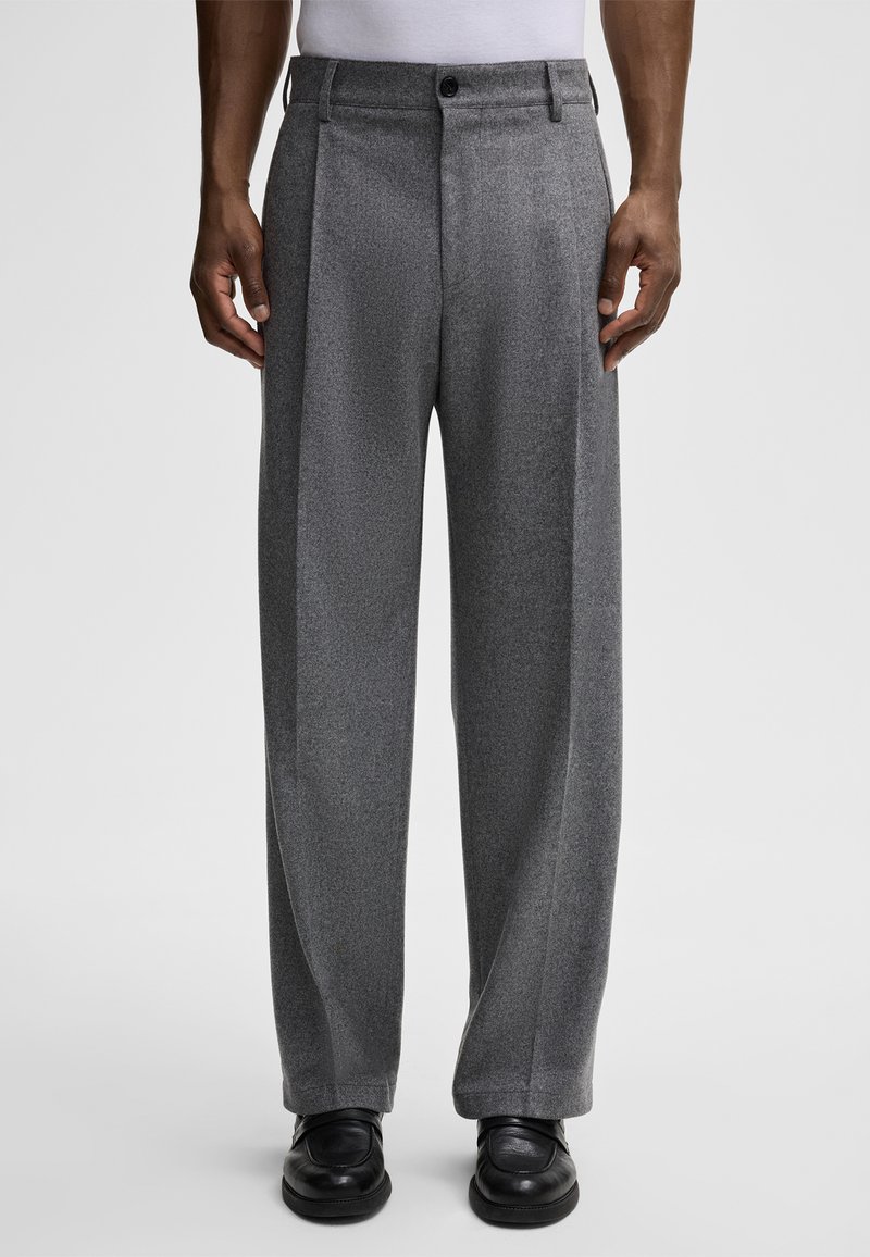 Szare spodnie w kant z fakturowanym wykończeniem, z zapięciem na guzik i szerokimi nogawkami, które zestawiono z czarnymi butami.