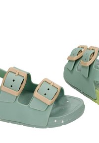 Paire de sandales vert clair à enfiler avec doubles boucles beiges et semelle tachetée, conçue pour un usage décontracté.