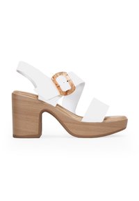 Sandales à talons hauts blanches avec de larges lanières, dotées d'une grande boucle translucide et d'un talon en bois. Matériau synthétique lisse.