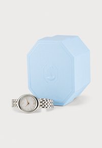 Silver watch with an oval face, textured silver dial, and a link bracelet, next to a light blue octagonal box with a swan logo.