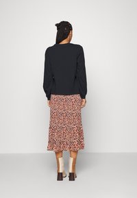 Schwarzes Langarmoberteil mit rundem Ausschnitt, kombiniert mit einem midi Rock in Schichten mit floralem Muster in verschiedenen Orangetönen und Rosa. Hellfarbene Blockabsätze.