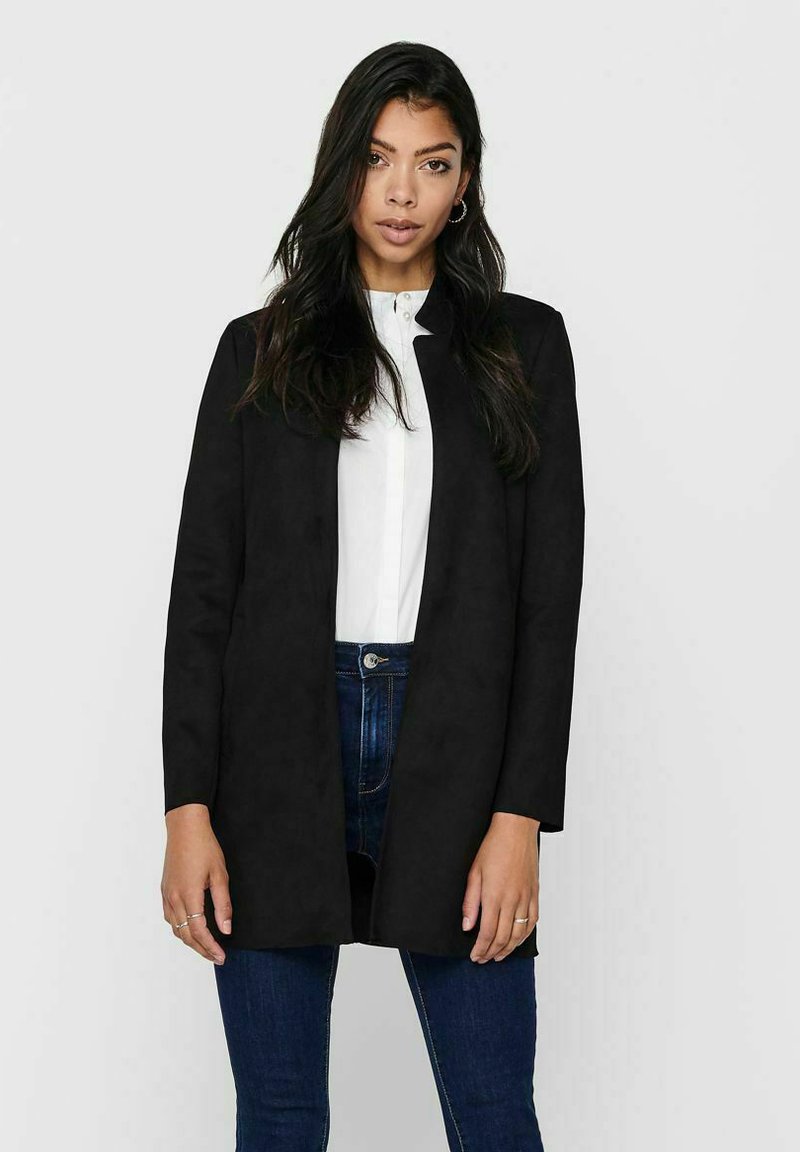 Blazer nero a maniche lunghe con una texture liscia e design aperto. Indossato sopra una camicia bianca, abbinato a jeans scuri.