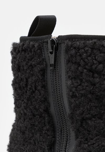 Botas pretas com um exterior texturizado e fofinho, painel lateral liso, fecho de correr e uma alça em laço na parte superior.