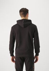 Felpa nera con cappuccio, maniche lunghe e polsini a coste. Realizzata in un tessuto morbido, presenta un design semplice e senza cuciture, con tasca a canguro.
