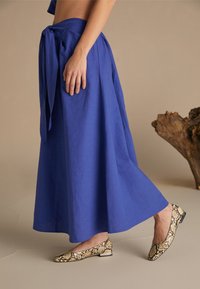 Blå, ankel-lang skjørt med knyttet liv, laget av lett stoff; kombinert med snakeskinnmønstrede balletflats med lav hæl.