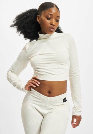 Hvit cropped langermet topp med subtile paisleymønstre, kombinert med matchende høyhårede leggings med en logotagg. Jevn tekstur.