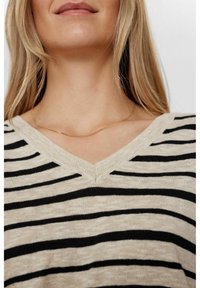 Beige- och svartsrandig tröja med V-ringning, tillverkad av ett strukturerat stickat material. Ett tunt guldhalsband är synligt.