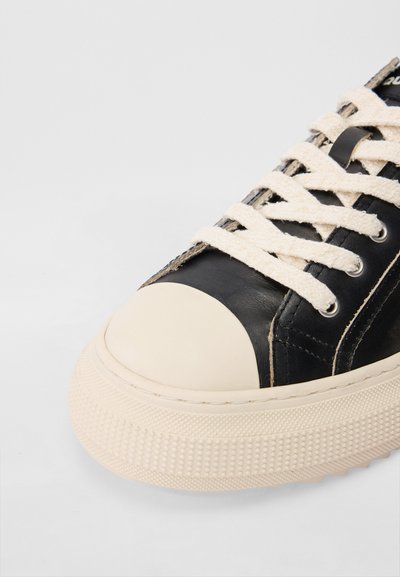 Schwarze Ledersneaker mit einer cremefarbenen Gummikappe und strukturierten, hellweißen Sohlen. Mit beigen Schnürsenkeln und Metallösen ausgestattet.