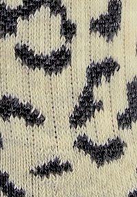 Gemusterter Strickstoff mit beigem Grund und unregelmäßigen schwarzen Flecken, die einen Leopardenlook erzeugen. Weiche Textur mit gerippten Details.
