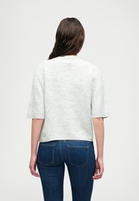 Grijze, kortekraag gebreide trui met een ronde halslijn en een zachte textuur, gecombineerd met donkerblauwe, aansluitende jeans. Eenvoudig en casual ontwerp.