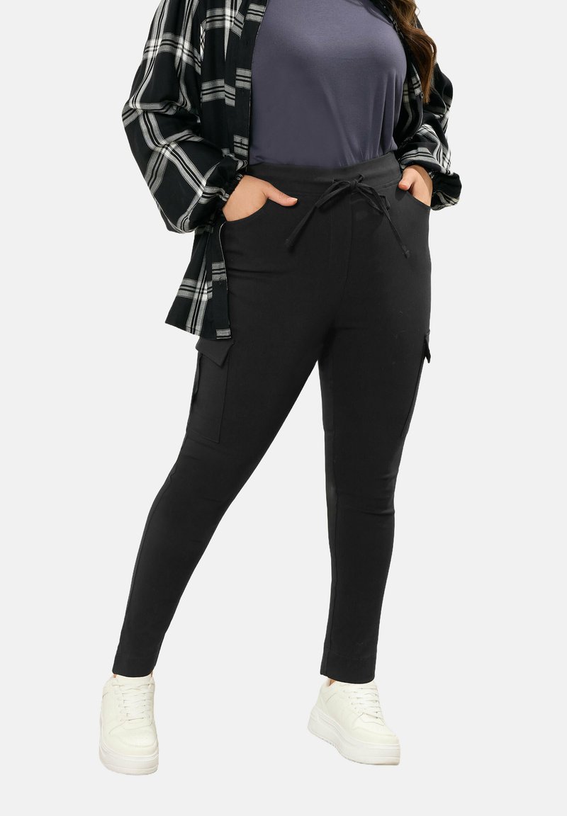 Mustat kapenevat housut, joissa on taskut, naru vyötäröllä ja sileä pinta, yhdistettynä harmaaseen yläosaan sekä musta-valkoiseen ruutupaitaan.