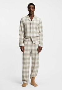 Beiges und hellbraunes kariertes Pyjam Set aus weichem Stoff. Enthält ein Hemd mit Knopfleiste und langen Ärmeln sowie eine Hose mit elastischem Bund.