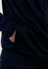 Chaqueta de chándal navy con una textura suave, que cuenta con un bolsillo lateral y puños de canalé. La tela es ligera y transpirable.