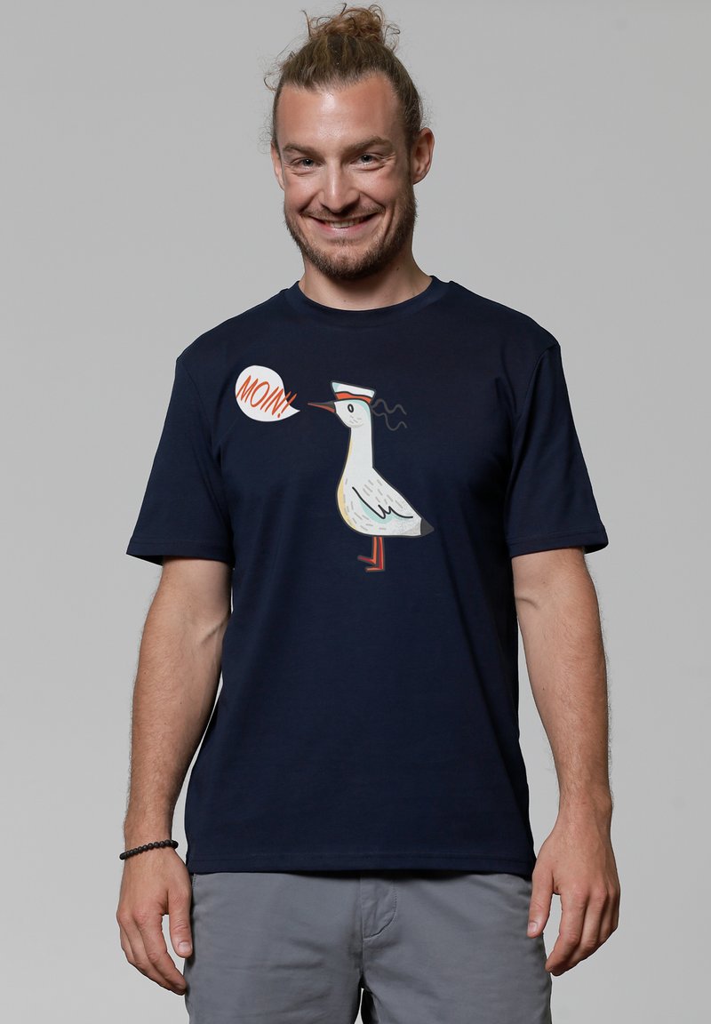 Navyblauwe katoenen t-shirt met een afbeelding van een witte vogel met een pet en het woord "Moin" in een spraakbel, korte mouwen, ontspannen pasvorm.