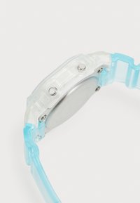 Montre transparente avec un boîtier clair et un bracelet bleu clair. Comprend un cadran rond argenté et deux boutons sur le côté.