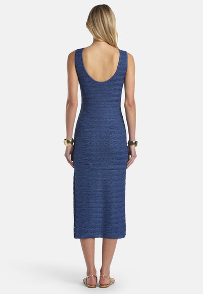 Femme portant une robe midi en crochet bleue sans manches avec un dos décolleté, des bracelets larges dorés et des sandales plates, debout de dos.