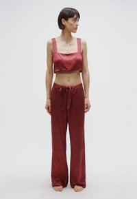 Punane satiinist kahetükkiline komplekt, mis sisaldab lühendatud topi laiade rihmadega ja mustrilisi laia säärega pükse, mis on vöökohtast paelaga seotud.