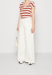 Rød og hvid stribet v-neck t-shirt, sat sammen med brede hvide denim bukser. Tilbehør med en lille hvid taske og sporty sko.