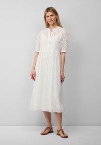 Vestido midi blanco con mangas abullonadas, tapeta de botones y patrón de ondas texturizado. Combinado con sandalias planas marrones. Diseño simple y ligero.