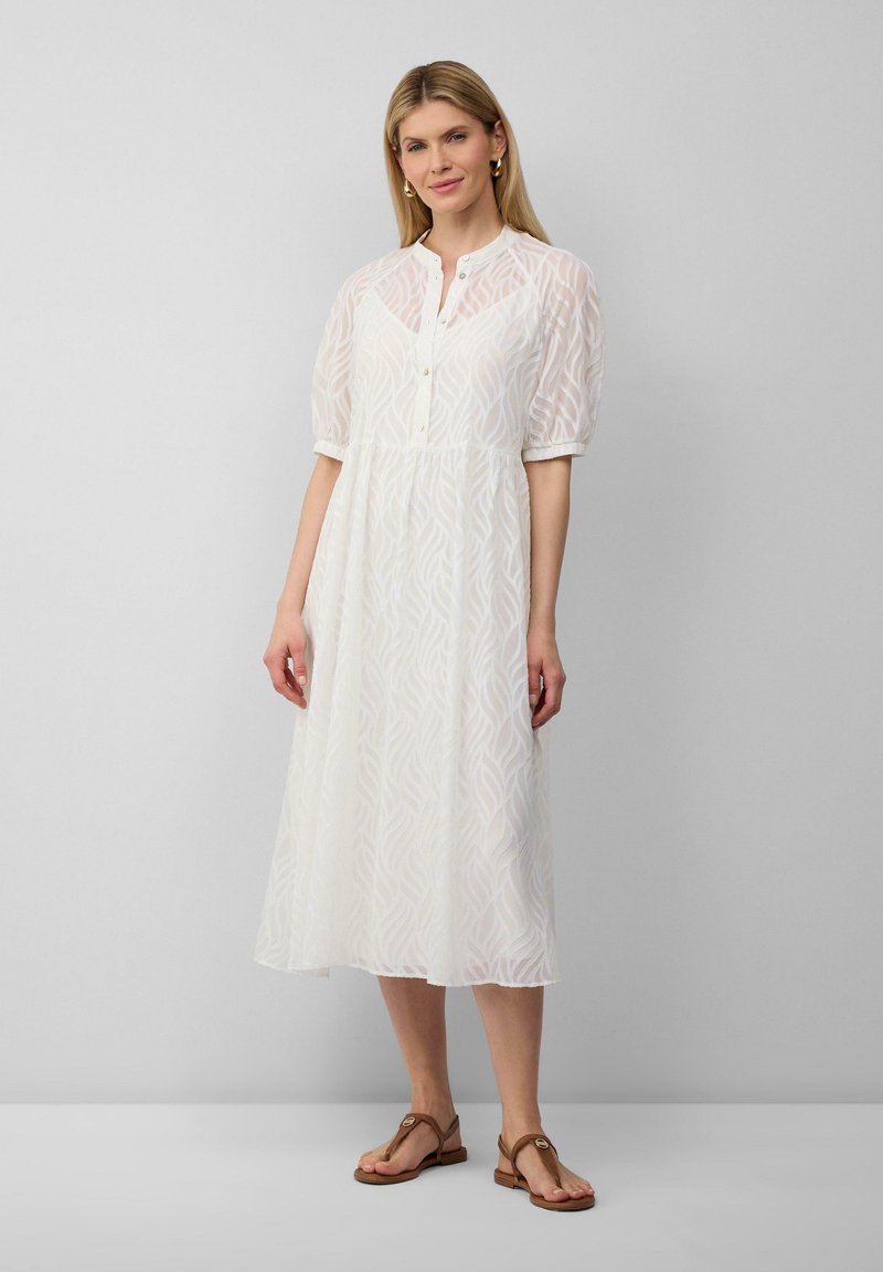 Vestido midi blanco con mangas abullonadas, tapeta de botones y patrón de ondas texturizado. Combinado con sandalias planas marrones. Diseño simple y ligero.