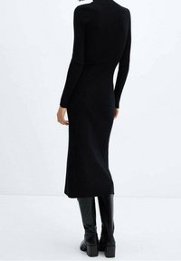 Robe noire en tricot côtelé avec des manches longues, longueur au genou et une silhouette ajustée. Associée à des bottes noires montantes.