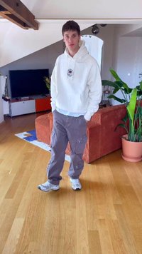 Casual outfit featuring a white hooded sweatshirt, grey cargo pants with pockets, and white sneakers with blue accents, set in a room with a plant.