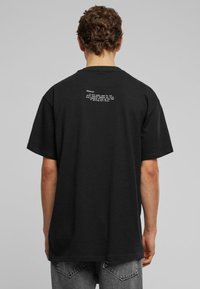 Sort bomulds T-shirt med korte ærmer, med hvid tekst på ryggen. Lige skåret stribe og afslappet pasform.
