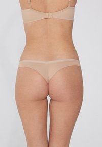 Beiges nahtloses BH- und String-Set aus weichem Material; verstellbare Träger, minimalistisches Design und glatte Textur ohne sichtbare Beschläge.