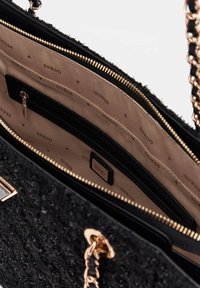 Schwarze Handtasche mit strukturiertem Design, goldener Kettenriemen, Logo-Applikationen und einem hellen Innenraum mit mehreren Fächern und einem Reißverschlussfach.