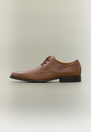 Brauner Herrenschuh aus Leder mit Schnürung vorne und schwarzer Sohle, seitlich auf hellem einfarbigem Hintergrund abgebildet.