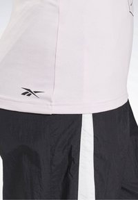 Light pink short-sleeve shirt with a fitted design, a black logo at the hem, paired with textured black pants featuring white side stripes.