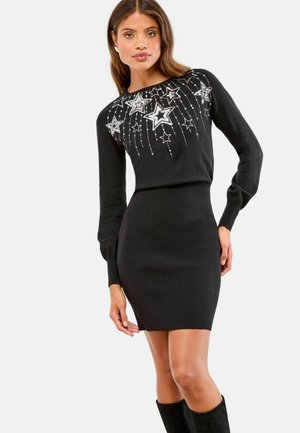 Czarna dzianinowa sukienka z długimi rękawami, dopasowanym krojem oraz srebrnymi gwiazdkami jako ozdobami z wiszącymi detalami na bodice.
