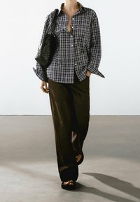 Koszula w kratę z guzikami w kolorze szarym i czarnym, zestawiona z szerokimi spodniami w kolorze ciemnego brązu oraz czarnymi sandałami na platformie, z plecioną czarną torebką.