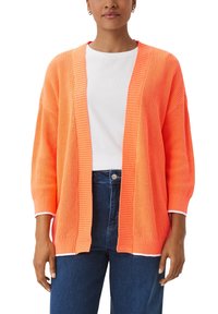 Strickjacke in kräftigem Koralle, offenem Vorderteil mit geripptem Muster und dreiviertel Ärmel. Getragen über einem weißen T-Shirt und blauen Jeans.