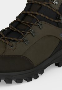 Κοντινή λήψη καφέ και μαύρου πεζοπορικού μποτάκι που δείχνει την υφή της σόλας, ανθεκτικούς γάντζους για τα κορδόνια και καφέ κορδόνια με σχέδια.