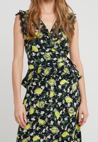 Svart wrap-top med citron- och blommönster, med volangärmar och peplum-fåll. Tillverkad av lätt tyg med en mjuk textur.