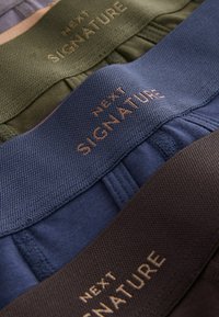 Három derékszalag szín: olívazöld, tengerészkék és sötétbarna. Mindegyiken arany színű "NEXT SIGNATURE" dombornyomott felirat látható. Láthatóan texturált felületek.