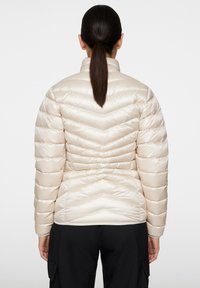Beżowa kurtka puchowa z wzorem w zygzaki, wysoki kołnierz i elastyczny pasek w talii. Gładka, błyszcząca tekstura; dopasowany krój.