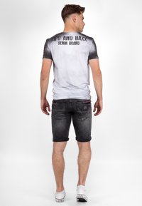 Grijze gradient t-shirt met een logo op de achterkant, gecombineerd met zwart denim shorts met omgeslagen zoom en witte sneakers. Soepele stof en casual pasvorm.